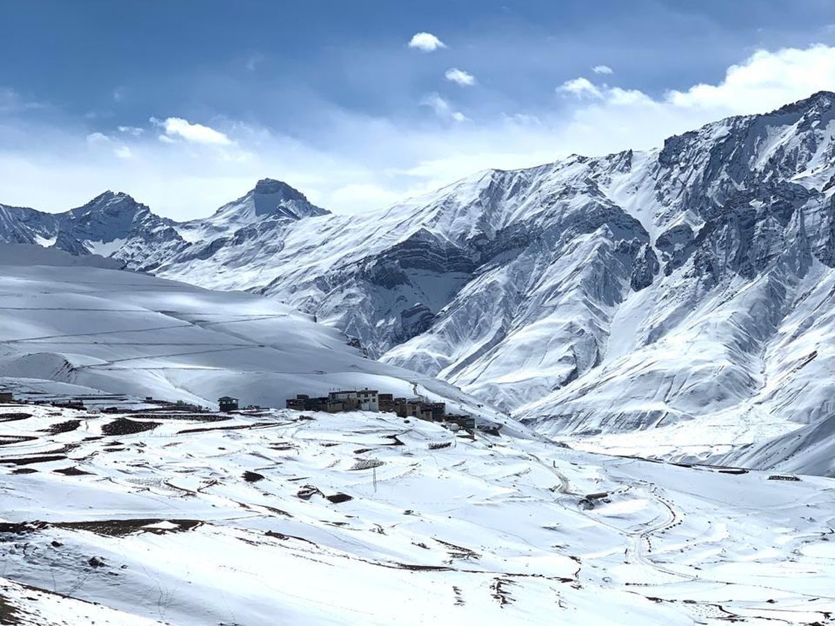 A small village nestled in a wide, snow-covered Himalayan valley, ringed by peaks
